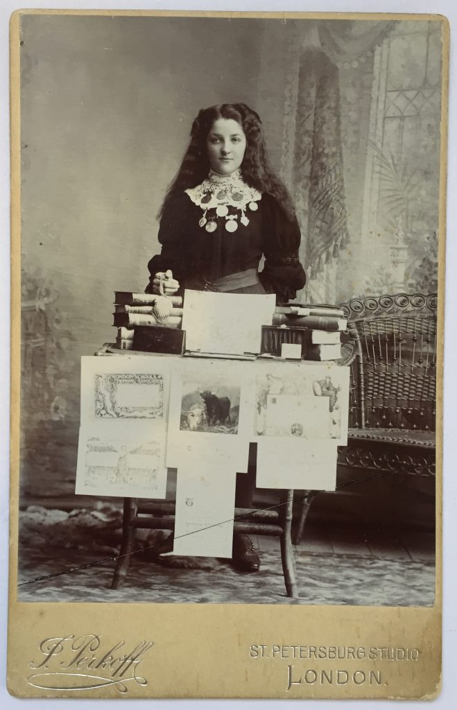 Photograph of a Victorian era school girl standing proudly with her many certificates of achievement and reward medals.