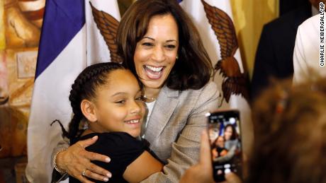 Kamala Harris hugs a Black girl, whose mother takes a cell phone picture.