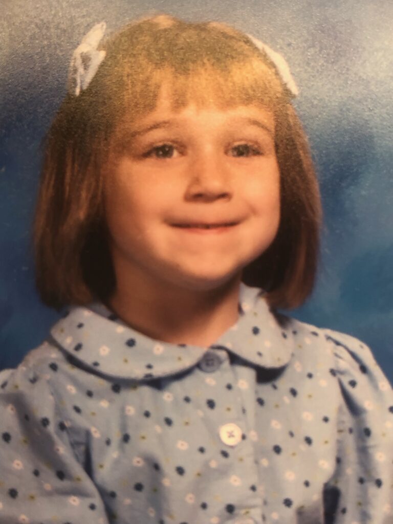 School photo of a young girl with two bows in her hair.