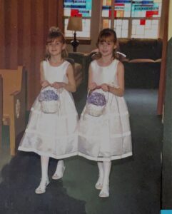 Two girls in white dresses walking down a church aisle with flower baskets.